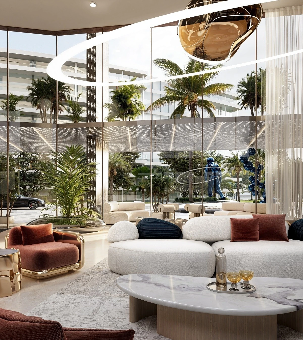 Contemporary lounge interior with rounded white sofas, rust-colored velvet armchair and cushions, a round marble coffee table holding a decanter and two glasses, a gold sculptural pendant light, and tall glass walls looking onto palm trees, low-rise buildings, a parked sports car and a blue astronaut-style statue.